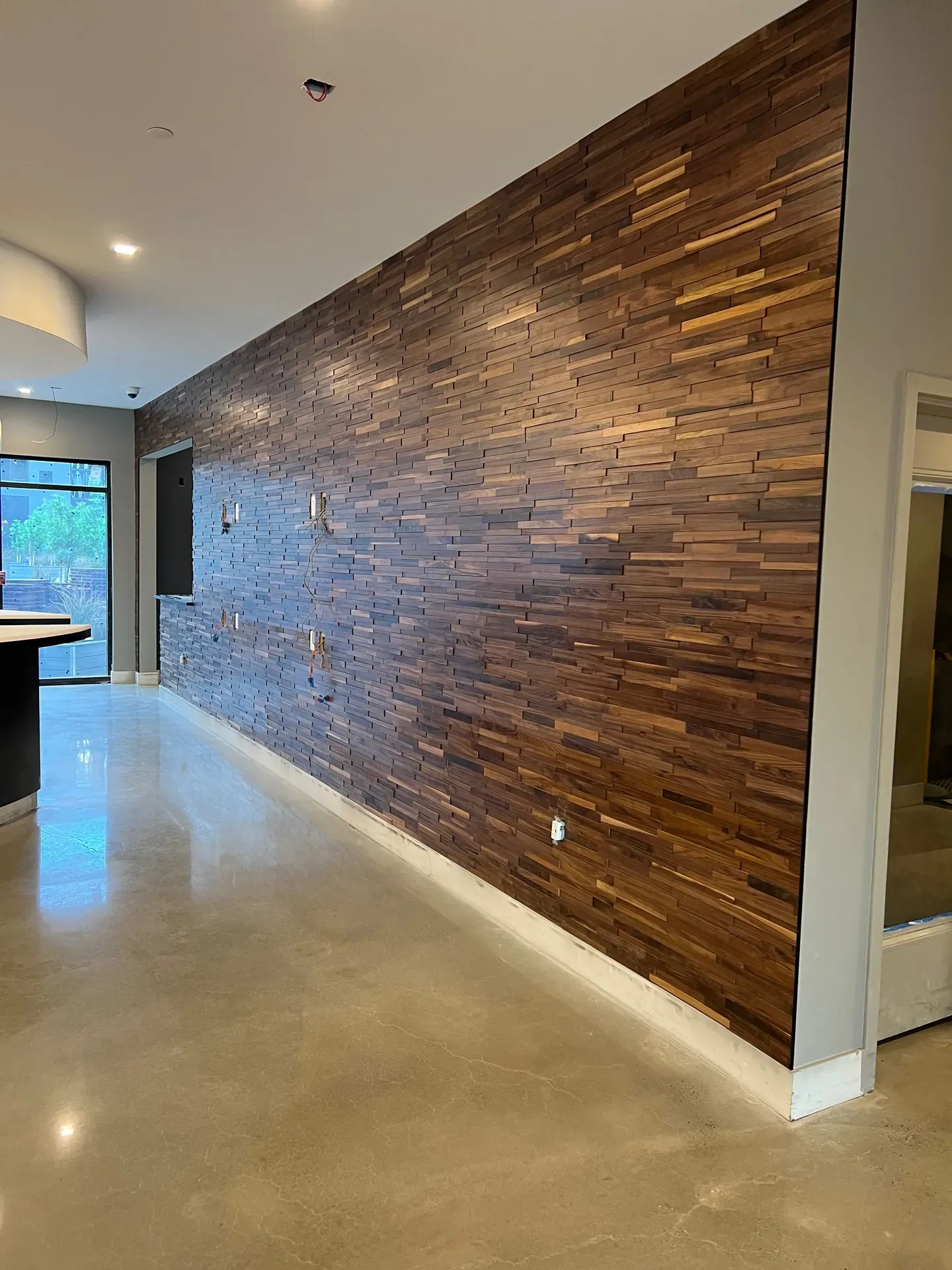 Full-height end-grain walnut feature wall in a modern commercial lobby, polished concrete floor, recessed ceiling lighting — specialty wood finish installation