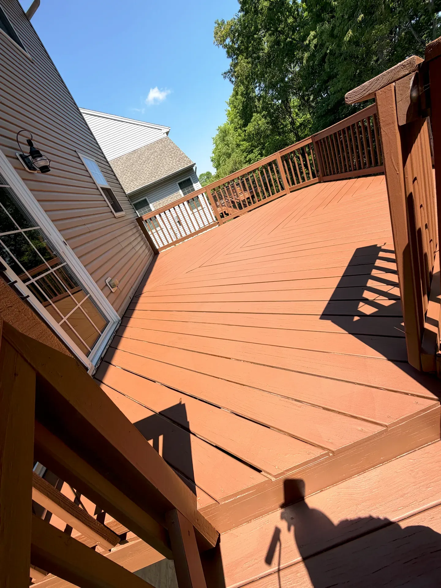 Backyard deck finished in a warm taupe-brown stain after a JL refinish — railing tops, deck boards, and stair treads all in matching tone, late-afternoon light raking across the boards