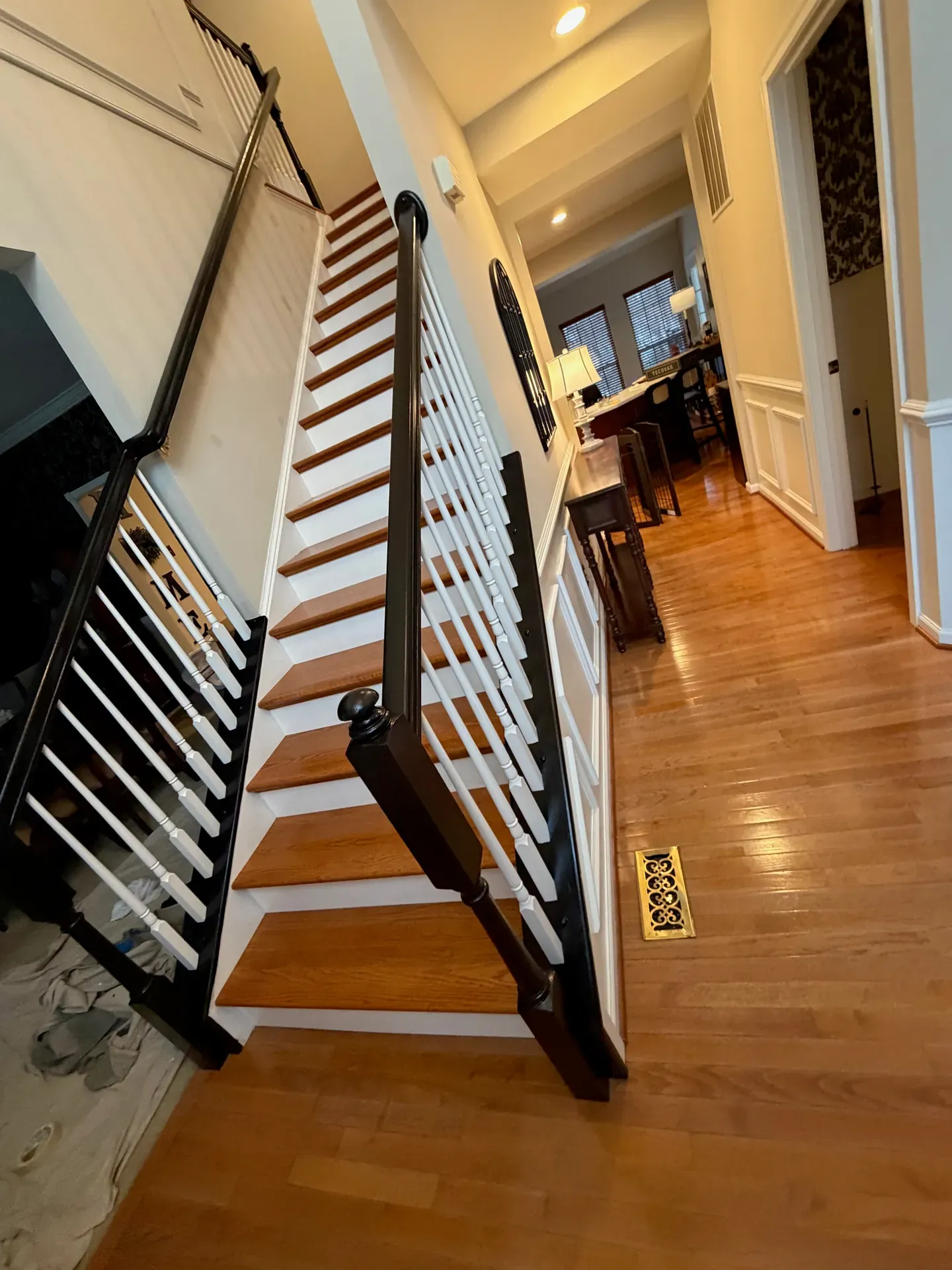 Open-tread residential staircase looking down to a hardwood entry — red oak treads, painted black newel and handrails, white spindles, view through to dining room with hardwood floor